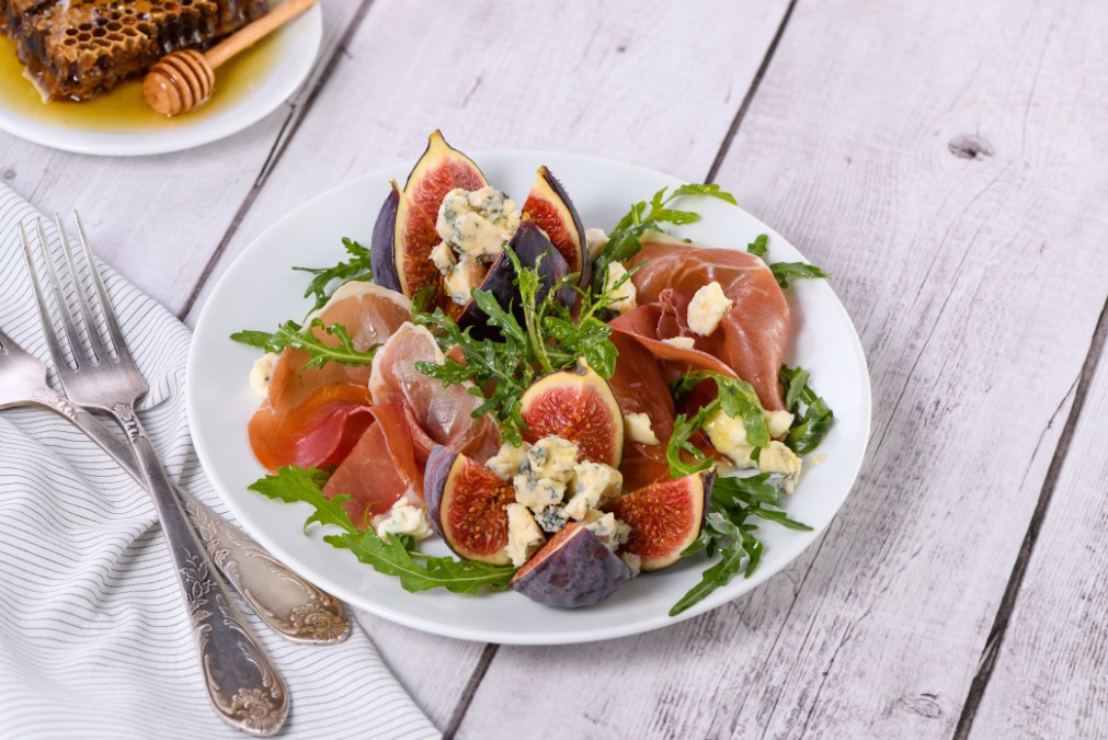 Délicieuse salade à la roquette accompagnée de figues roties et de tranches de jambon cru.